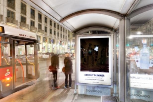 Eine Bushaltestelle mit Werbung für „Absolut Glimmer“ und wartenden Passanten.