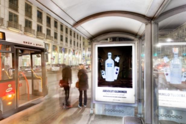 Eine Bushaltestelle mit Werbung für „Absolut Glimmer“ bei Nacht.