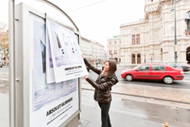 Eine Frau befestigt ein „Absolut Glimmer“-Poster an einer Bushaltestelle in Wien.