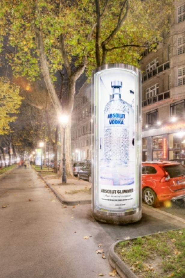 Eine beleuchtete Werbesäule für Absolut Vodka steht am Straßenrand.