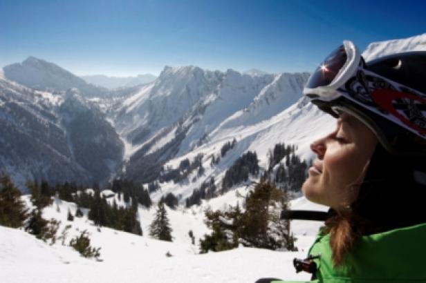 Eine Skifahrerin genießt die Sonne vor einer verschneiten Berglandschaft.
