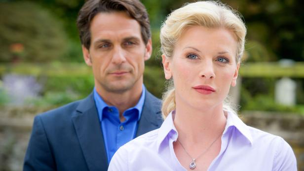 Eine blonde Frau mit einem Mann im Hintergrund.