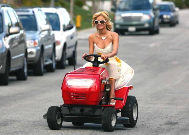 Paris Hilton fährt auf einer roten Aufsitzrasenmähermaschine eine Straße entlang.
