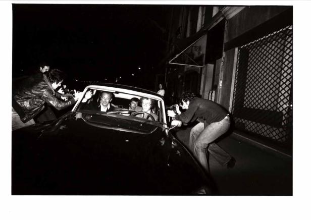 Paparazzi fotografieren eine Gruppe von Personen in einem Auto.