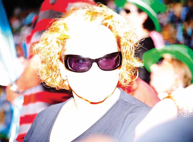 Eine Frau mit lockigem, blondem Haar und Sonnenbrille steht in einer Menschenmenge.