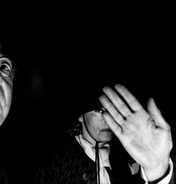 Eine Frau hält ihre Hand vor ihr Gesicht, während ein Mann links im Dunkeln steht.