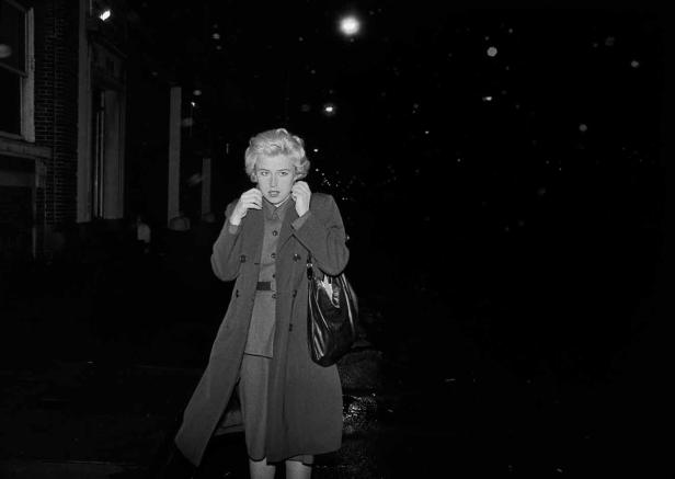 Eine Frau in Mantel und Handtasche steht nachts auf der Straße.