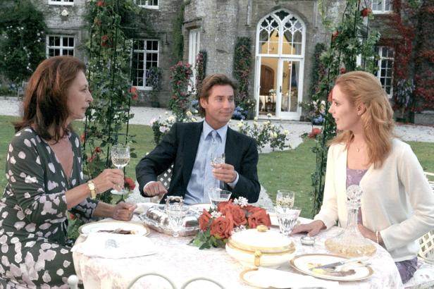 Drei Personen sitzen an einem Tisch im Garten eines Herrenhauses und trinken Wein.