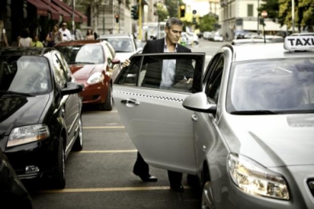 Ein Mann im Anzug steigt aus einem Taxi auf einer belebten Straße.