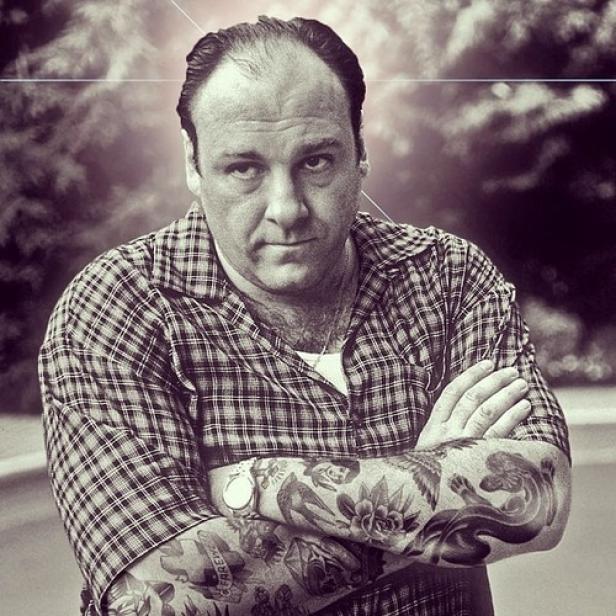 Ein Schwarz-Weiß-Porträt von James Gandolfini mit verschränkten, tätowierten Armen.