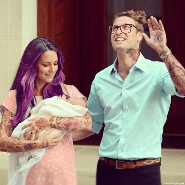 Ein Paar mit Tattoos und einem Baby vor einem Gebäude.