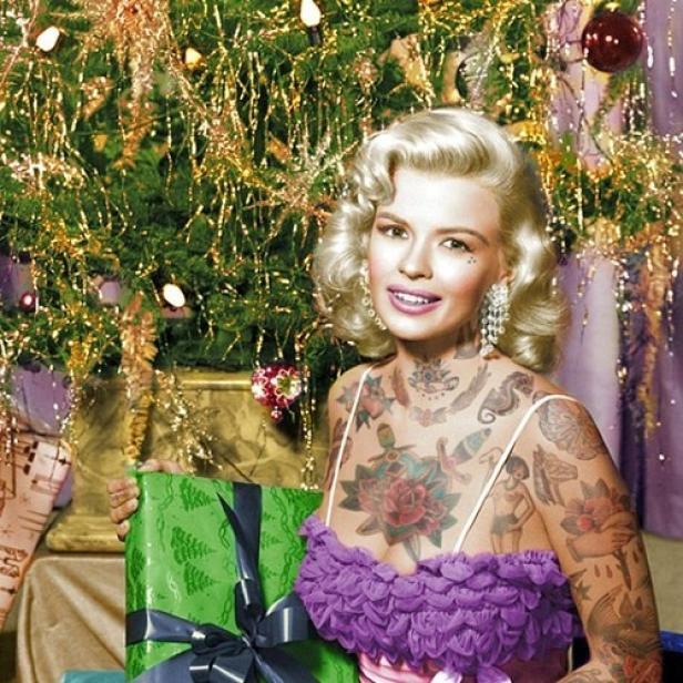 Eine tätowierte Frau im Stil von Marilyn Monroe hält ein Weihnachtsgeschenk vor einem Weihnachtsbaum.