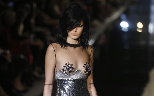 Ein Model mit dunklen Haaren trägt ein silbernes Paillettenkleid mit transparentem Oberteil.