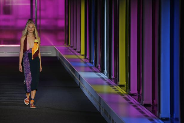Ein Model läuft in einem farbenfrohen Kleid über einen Laufsteg.