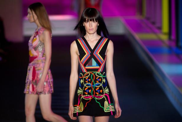 Eine Frau präsentiert ein schwarzes Kleid mit bunten, geometrischen Mustern auf einem Laufsteg.