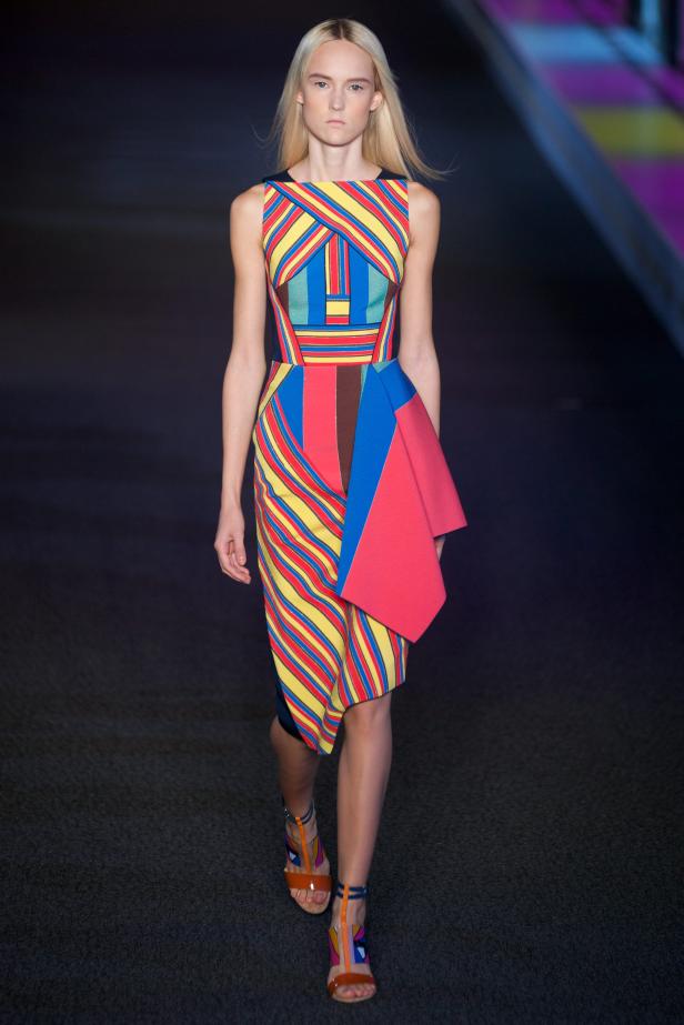 Eine Frau auf dem Laufsteg präsentiert ein farbenfrohes, geometrisch gemustertes Kleid.