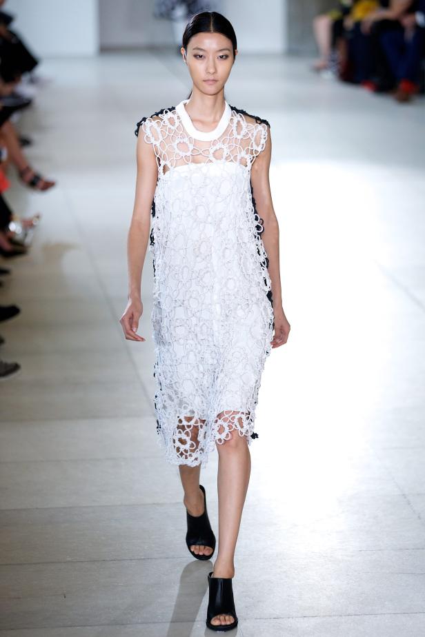 Eine Frau präsentiert ein weißes Kleid mit Lochmuster auf einem Laufsteg.