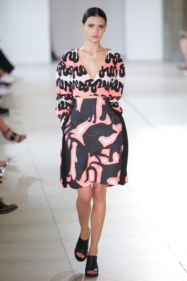 Eine Frau präsentiert ein Kleid mit einem Muster aus stilisierten Katzen auf einem Laufsteg.