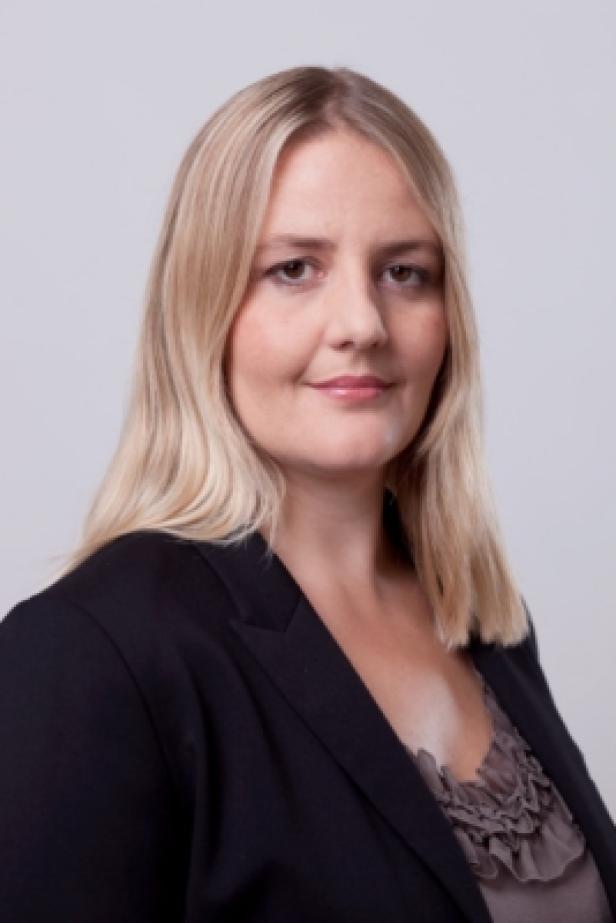 Eine Frau mit blonden Haaren und einem schwarzen Blazer lächelt in die Kamera.