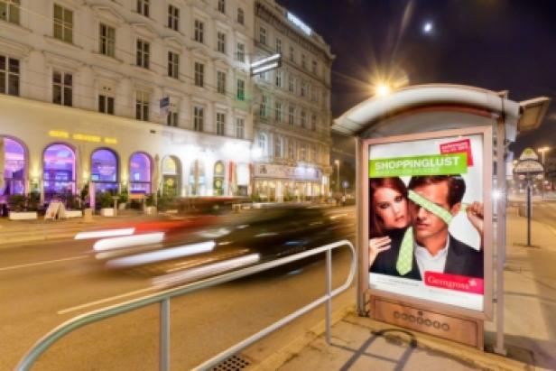 Eine Bushaltestelle mit Werbung für „Shoppinglust“ von Gerngross bei Nacht in Wien.
