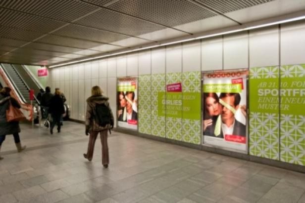 In einer U-Bahn-Station gehen Menschen an Werbeplakaten vorbei.