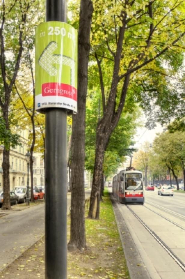 Eine Straßenbahnhaltestelle in Wien mit einem Wegweiser zu einem Einkaufszentrum.