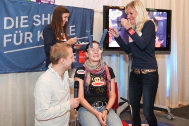 Eine Frau nimmt an einem Spiel teil, bei dem ihr von zwei Personen Essen in den Mund gefüllt wird.