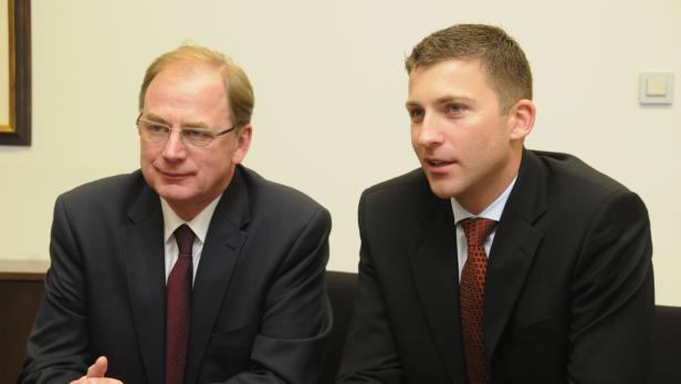 Zwei Männer in Anzügen sitzen nebeneinander.