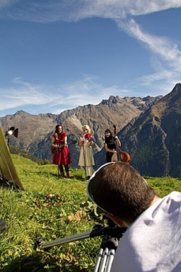 Drei Musikerinnen posieren mit ihren Instrumenten vor einer Bergkulisse für einen Videodreh.