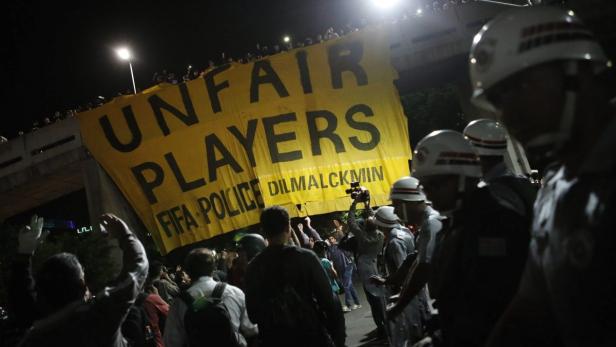 Eine Menschenmenge demonstriert mit einem gelben Banner mit der Aufschrift „Unfair Players FIFA Police“.