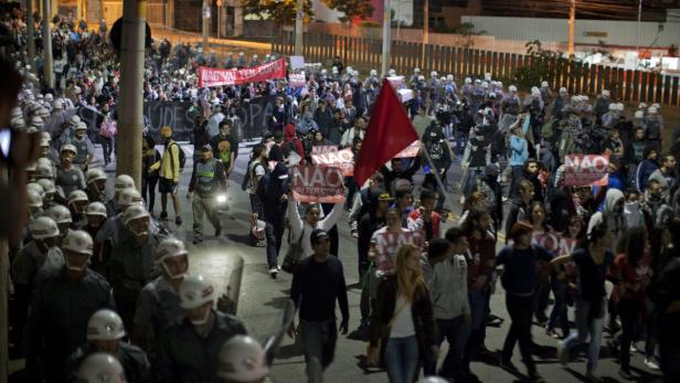 Eine Menschenmenge demonstriert mit Schildern und einer roten Flagge auf einer Straße.