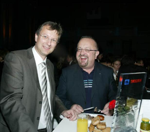 Zwei Männer stehen an einem Tisch mit Speisen und Getränken.