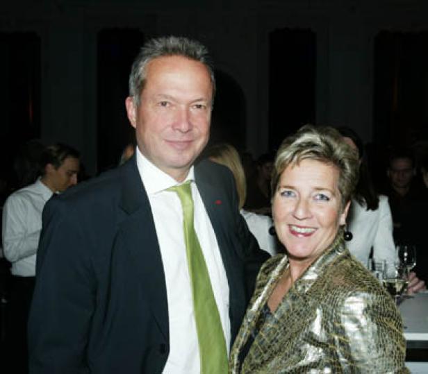 Ein Mann im Anzug mit grüner Krawatte und eine Frau in einer goldenen Jacke posieren für ein Foto.