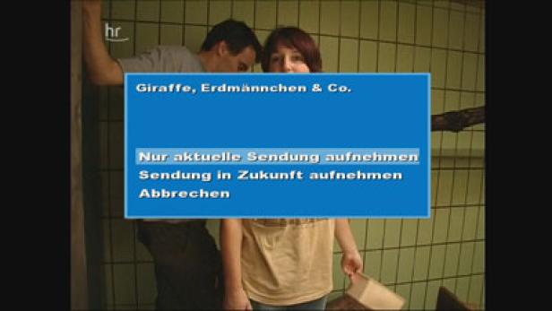 Ein Mann und ein Kind stehen vor einem Bildschirm mit der Aufschrift „Giraffe, Erdmännchen & Co.“.