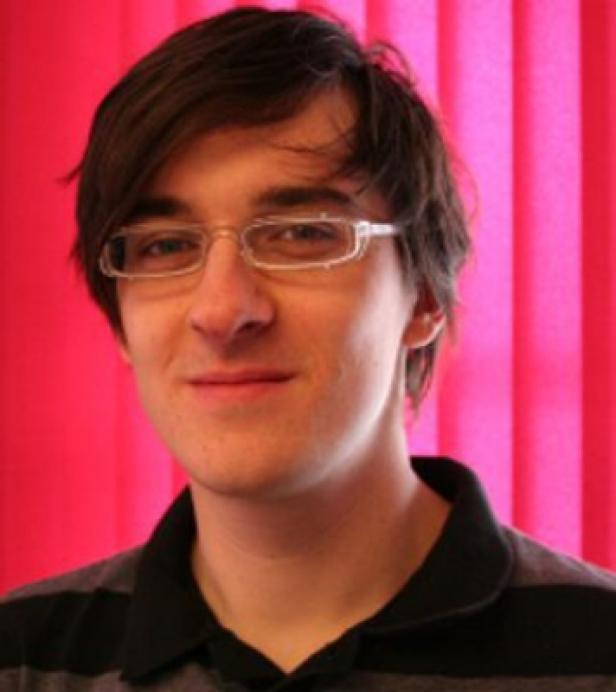 Ein junger Mann mit Brille lächelt in die Kamera.