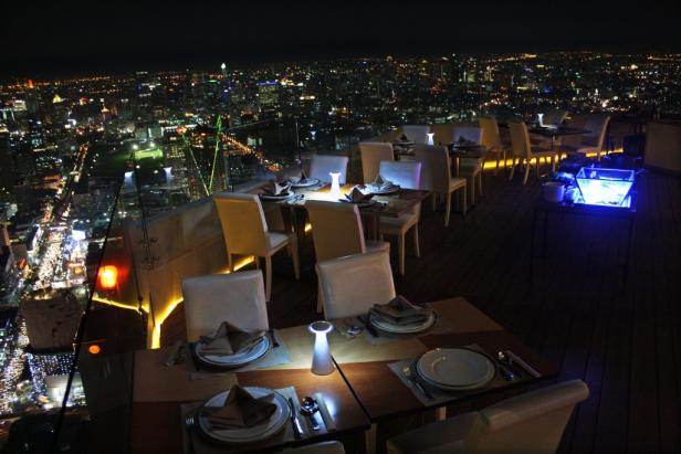 Ein Restaurant auf einem Dach mit Blick auf eine beleuchtete Stadt bei Nacht.