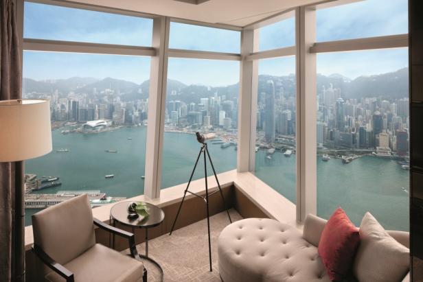 Ein Zimmer mit Blick auf die Skyline von Hongkong und das Meer durch ein großes Fenster.