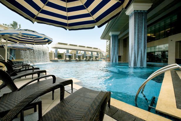 Ein luxuriöser Poolbereich mit Liegestühlen und blau-weiß gestreiften Sonnenschirmen.