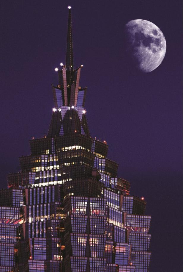 Ein Wolkenkratzer erstreckt sich nachts vor einem großen Mond in den Himmel.