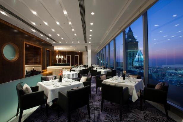 Ein elegantes Restaurant mit Tischen am Fenster und Blick auf die Stadt bei Dämmerung.