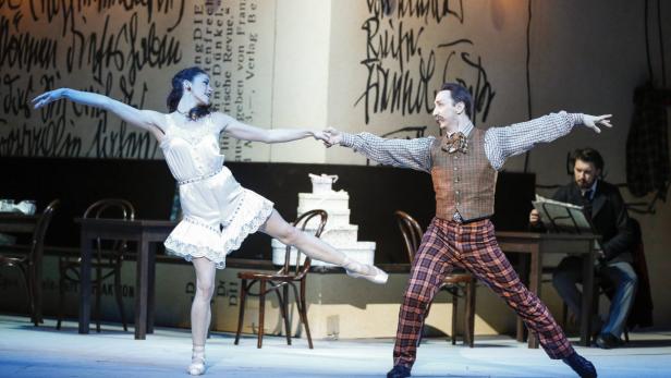 Eine Ballerina und ein Mann im Anzug tanzen auf einer Bühne.