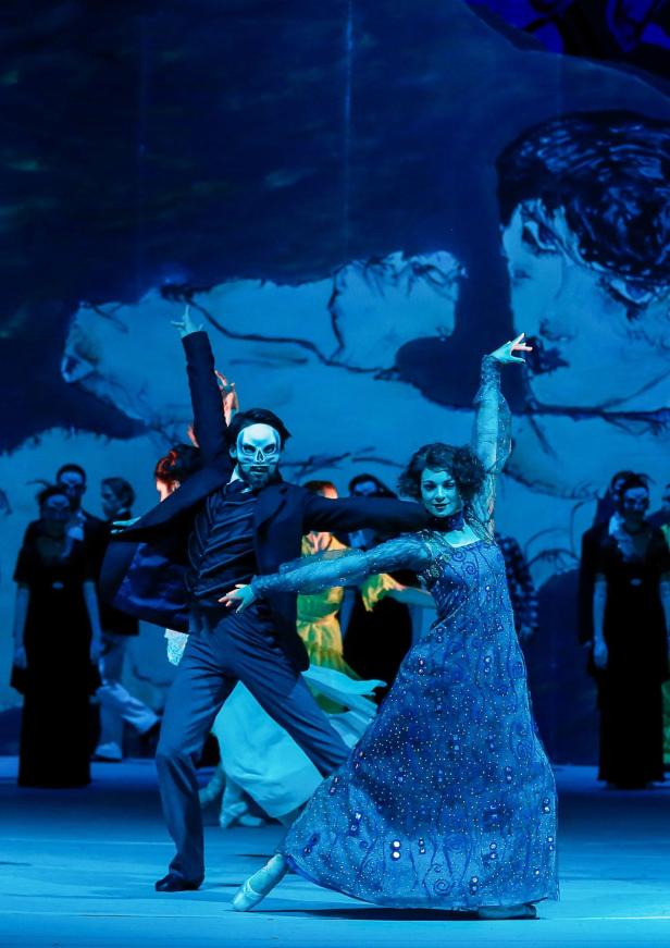 Ein maskierter Tänzer und eine Tänzerin in einem blauen Kleid tanzen auf einer Bühne.