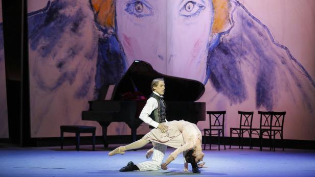 Ein Ballett-Tänzerpaar auf einer Bühne mit einem Klavier und einem gemalten Hintergrund.