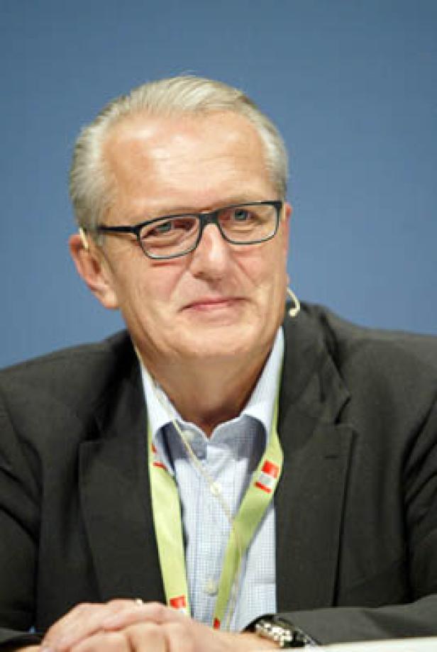 Ein Mann mit Brille und Anzug vor einem blauen Hintergrund.