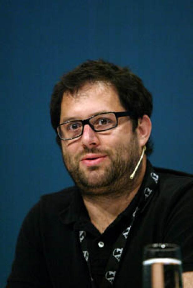 Ein Mann mit Brille und Bart trägt ein schwarzes Hemd und ein Lanyard.