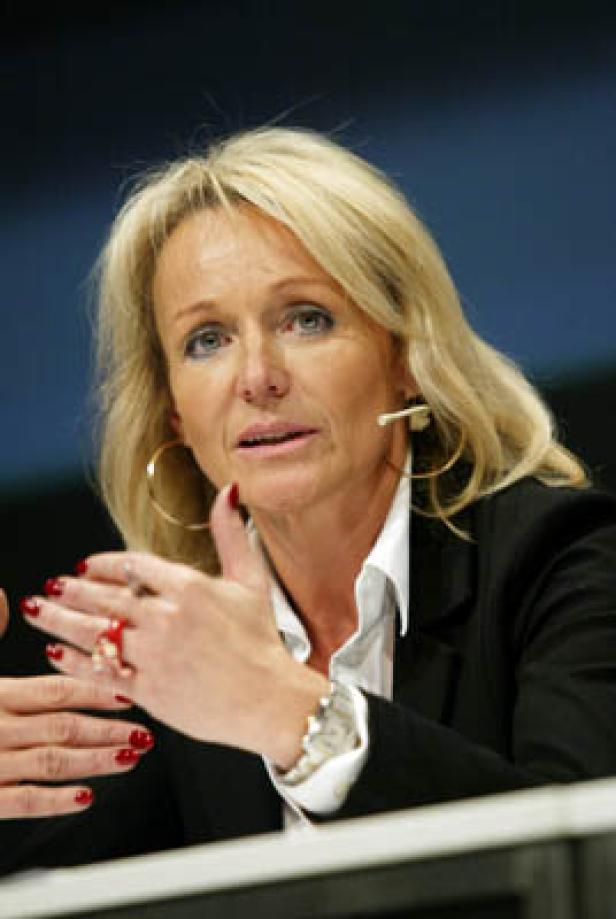 Eine blonde Frau gestikuliert während einer Präsentation.