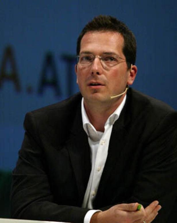 Ein Mann mit Brille und Mikrofon sitzt an einem Tisch.