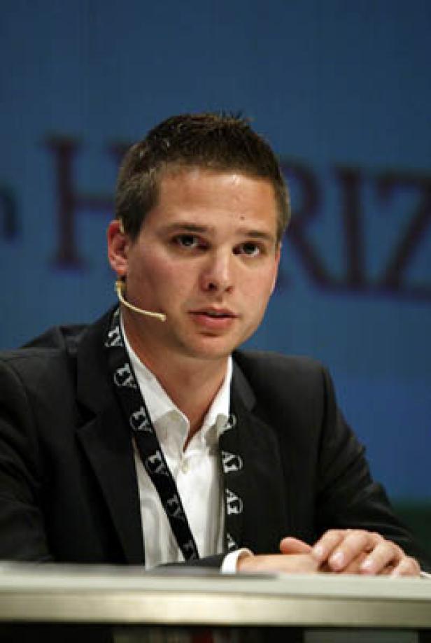 Ein Mann mit Mikrofon und Anzug sitzt an einem Tisch.