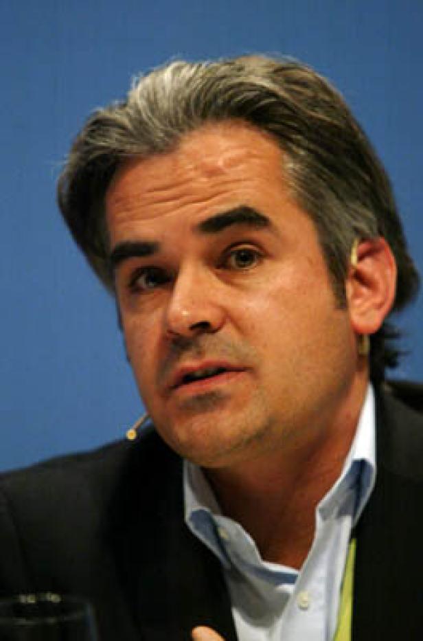 Ein Mann mit grau meliertem Haar spricht vor einem blauen Hintergrund.