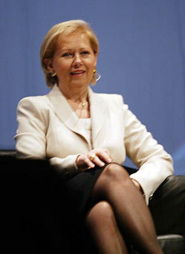 Eine blonde Frau sitzt in einem Sessel und lächelt.
